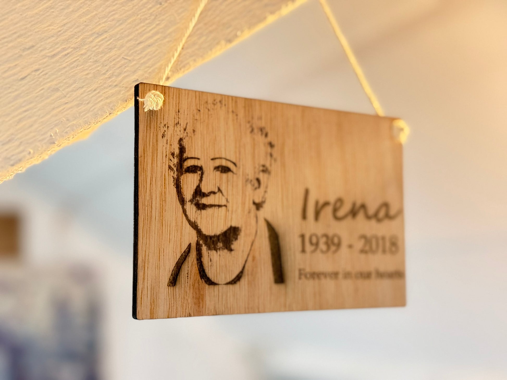 Wooden plaque with engraved portrait and text, hanging against a blurred background.